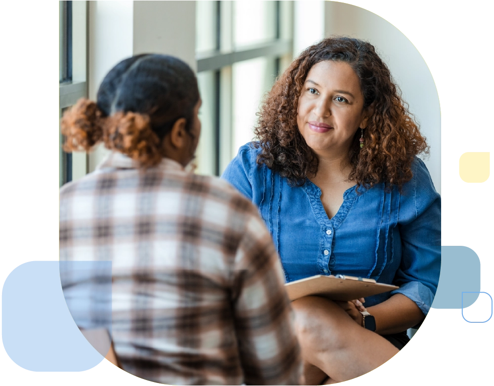 Two women in casual clothing having a discussion. One is a mental health professional, listening intently.