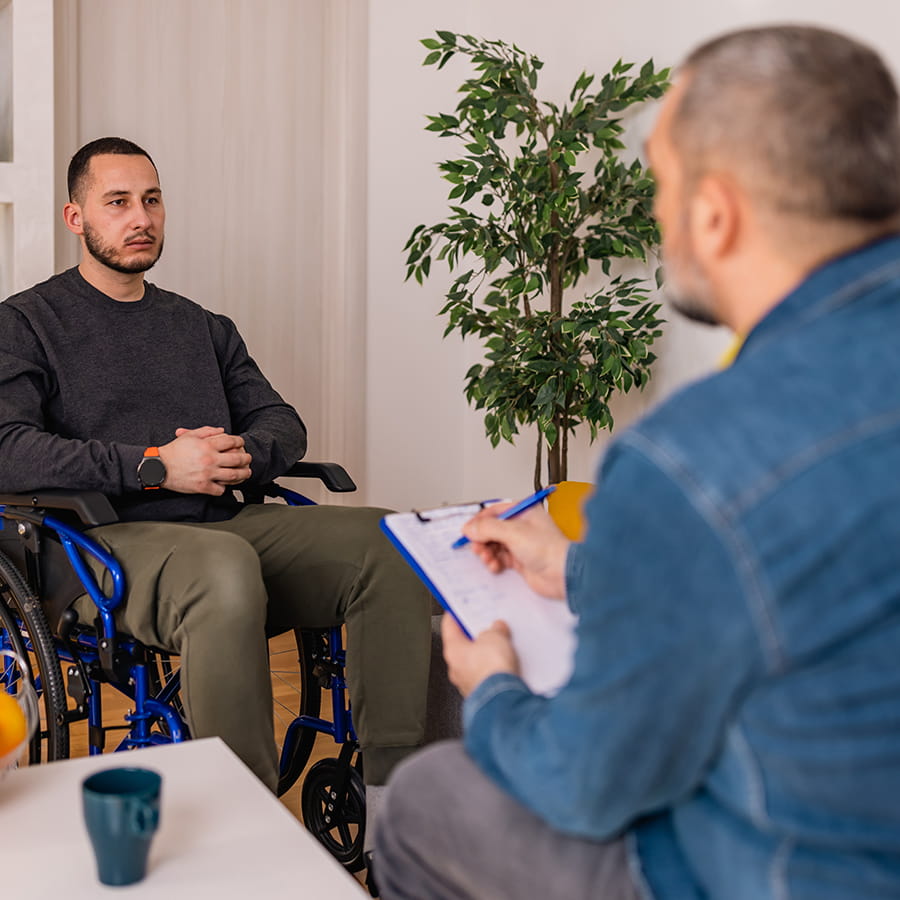 a young man in a wheelchair receives counseling from rehabilitation counselor wearing jean jacket back of head photo with man in wheelchair slightly blurred