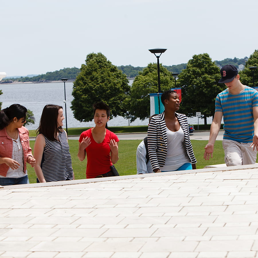 students of diverse ethnic backgrounds walking up steps of campus with ocean front in the background
