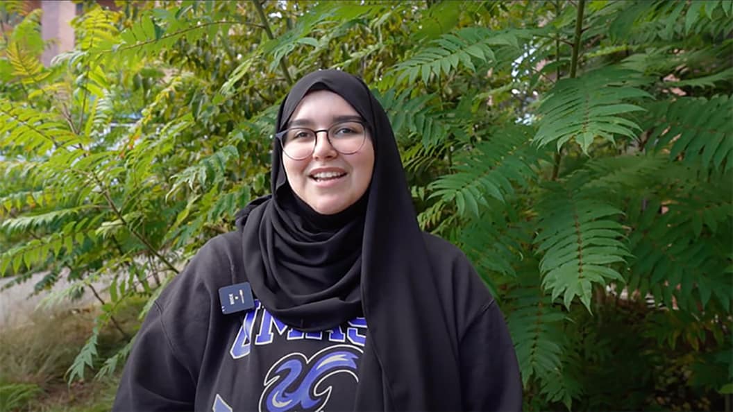 Student, Balsam, standing in front of green leaves.
