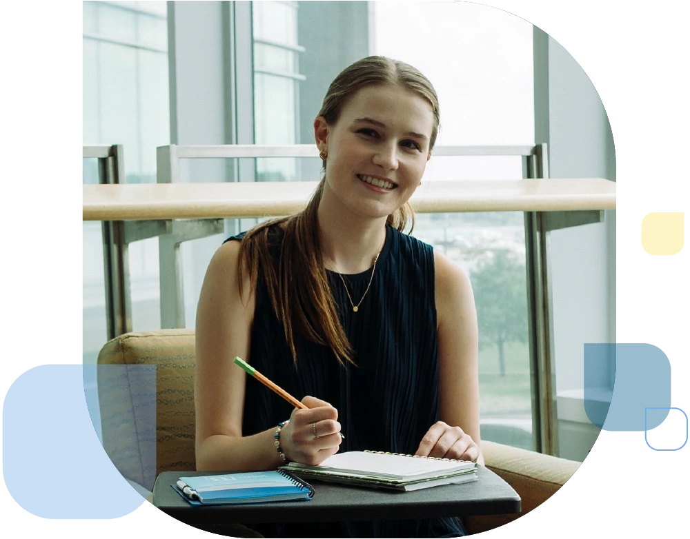 Graduate student working at desk in front of windows.