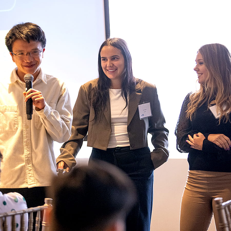 student with microphone at BEST Boston event as other students look on, backlighting from window