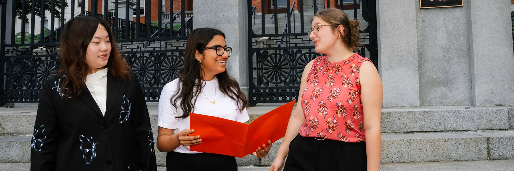 3 students read a folio in front of the MA statehouse.