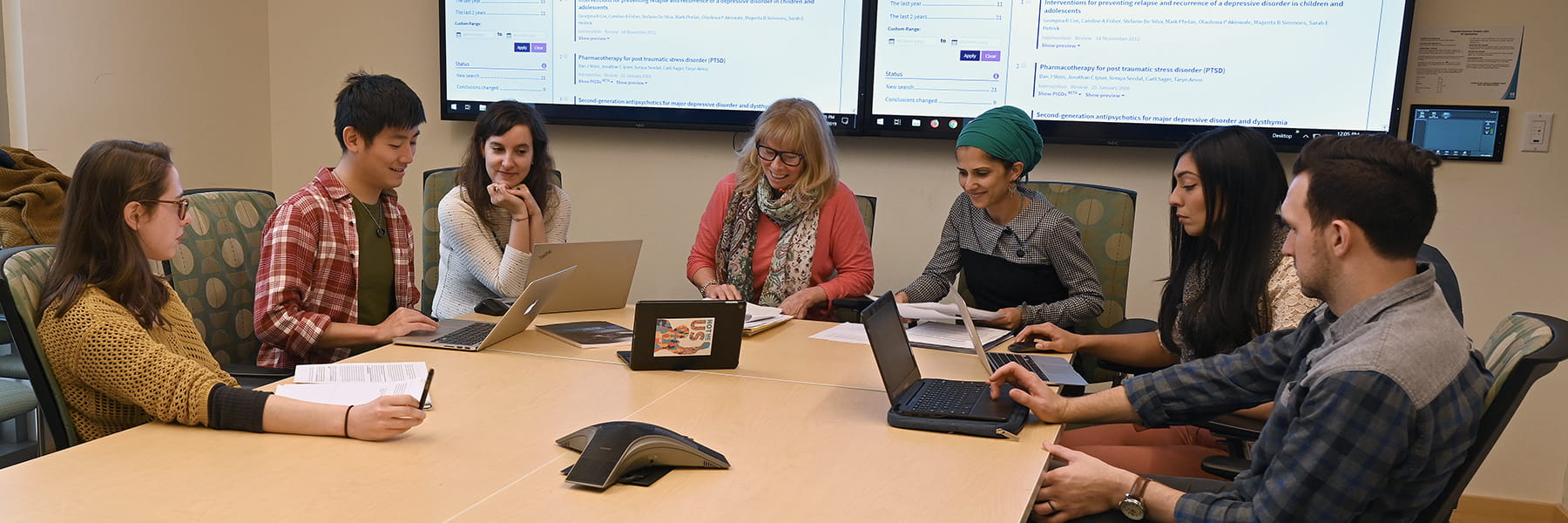 Staff & students talk around a seminar table.