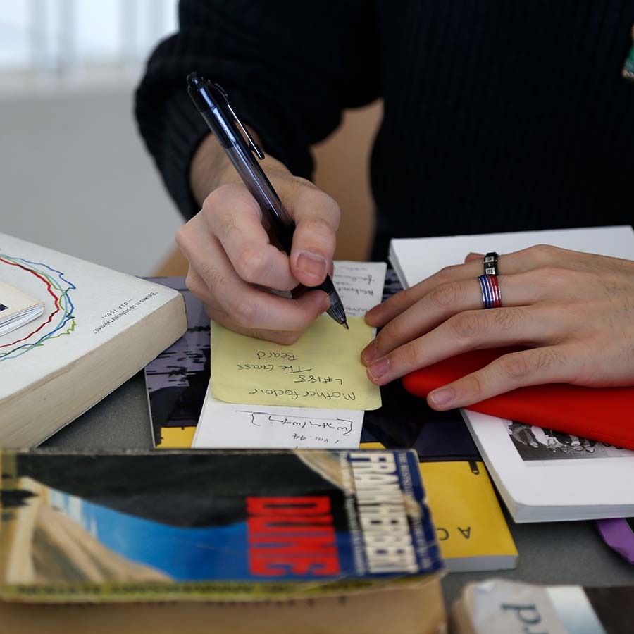 hand holding pen writing surrounding by books