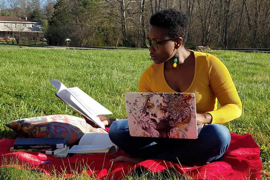 Student Margaret Gatonye works on laptop outside sitting on lawn.