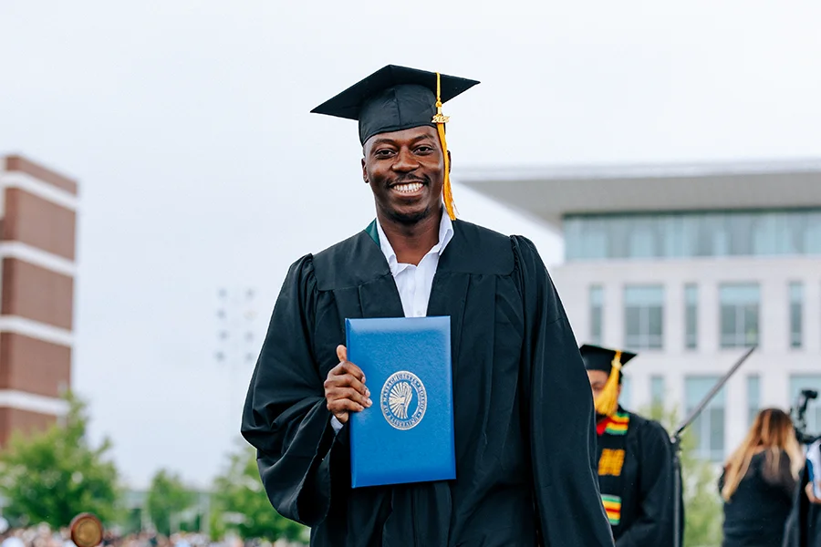 Student smiles and holds diploma on the stage on the Campus Center Lawn.