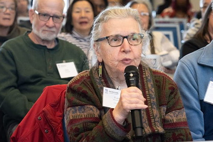 older woman holds mike and speaks at pension action fraud summit.