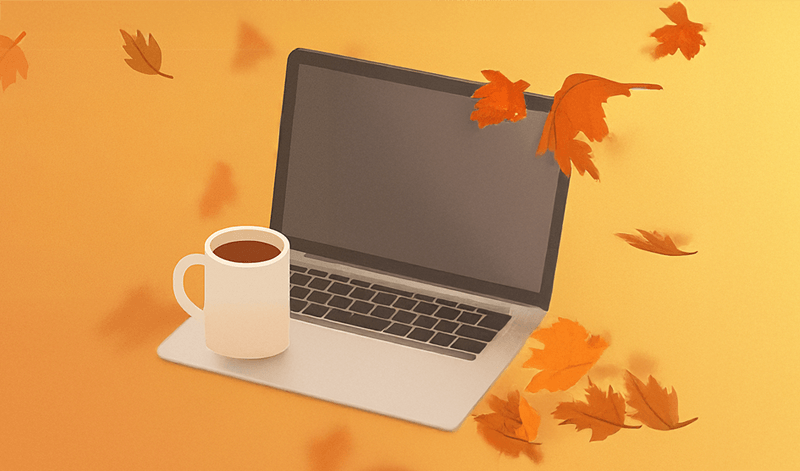 A laptop with a coffee on it and leaves fall around it