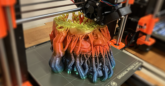 A 3D object is being printed that resembles a head in vibrant colors of red and purple.