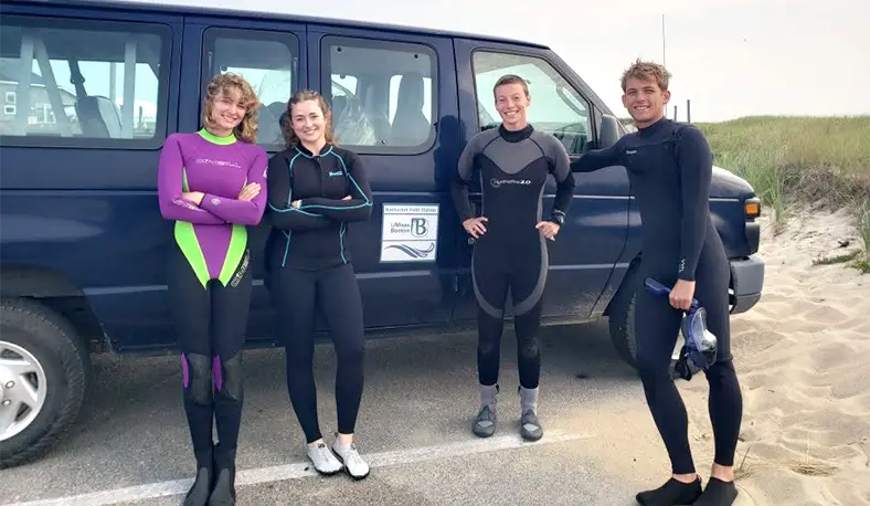 2026 summer interns in wetsuits pose by official field station van.