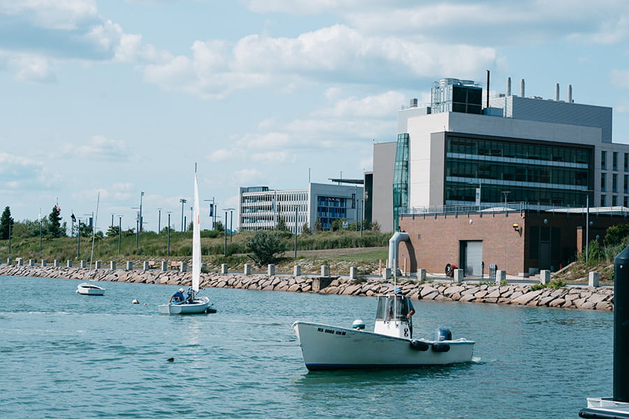 A view of the UMass Boston campus from the waters of Savin Hill Cove, showing the pumphouse, the ISC, and several boats.