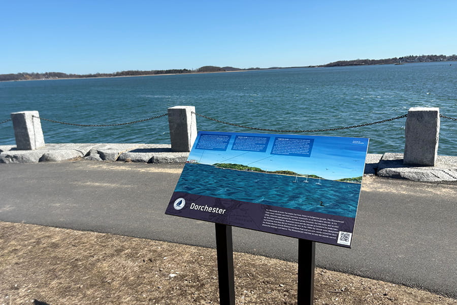 A sign along the Harborwalk, illustrated by a UMass Boston student, explains the islands of the Boston Harbor, which can be seen in the distance.
