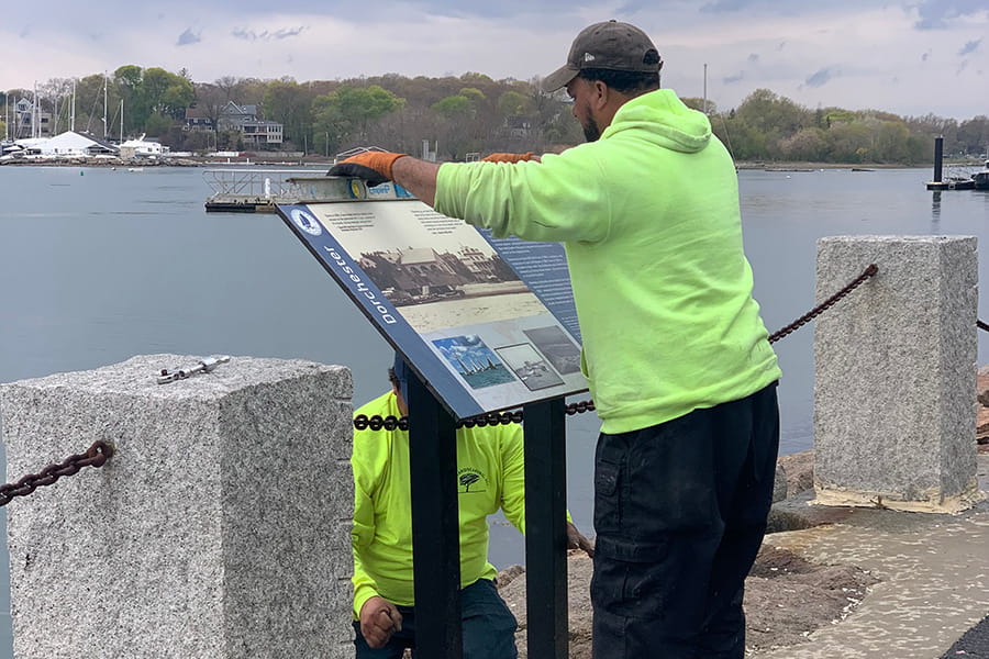 Workers install new signage along the Harborwalk near UMass Boston.