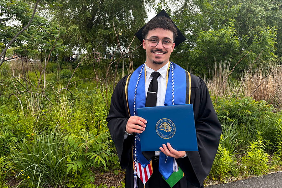 Emanuel Da Silva, a 2026 graduate, poses in front of verdant greenery