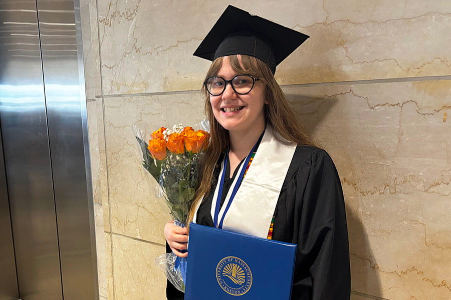Rhiannon Lecuyer, a 2026 graduate, stand smiling in the Campus Center, holding a bouquet of flowers.