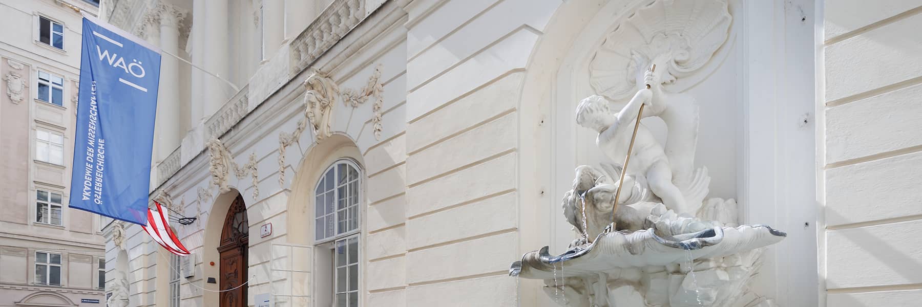 Close-up of outside white Austrian Academy of Sciences building and marble statue.