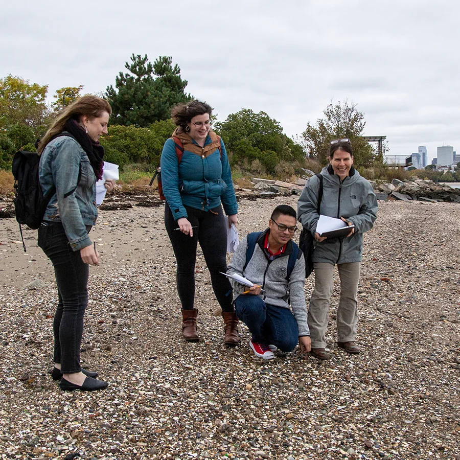 Students carrying clipboards examine shore of Carson Beach Boston.